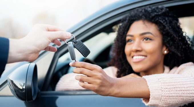 A woman on the drivers side of a vehicle accepting car keys from the hand of a person standing at the vehicle